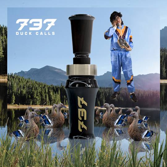 Black 737 duck call surrounded by decoys at a lake with mountains and forest, person in blue jumpsuit floating above