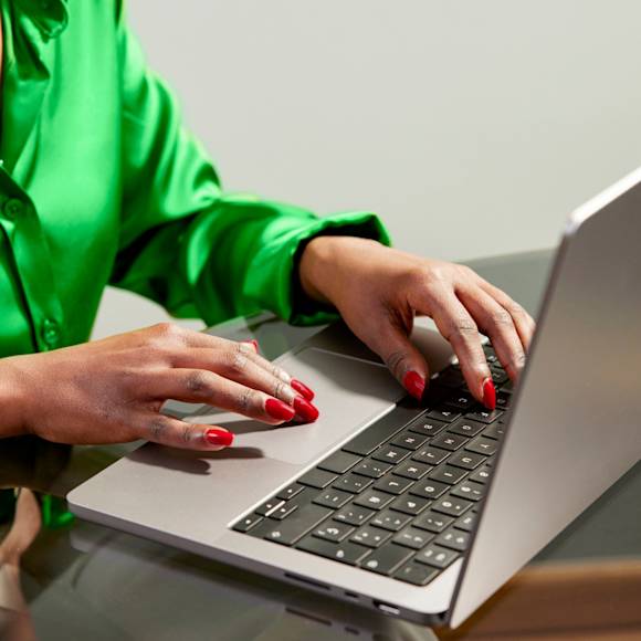 Person with green shirt and red nails typing on a laptop