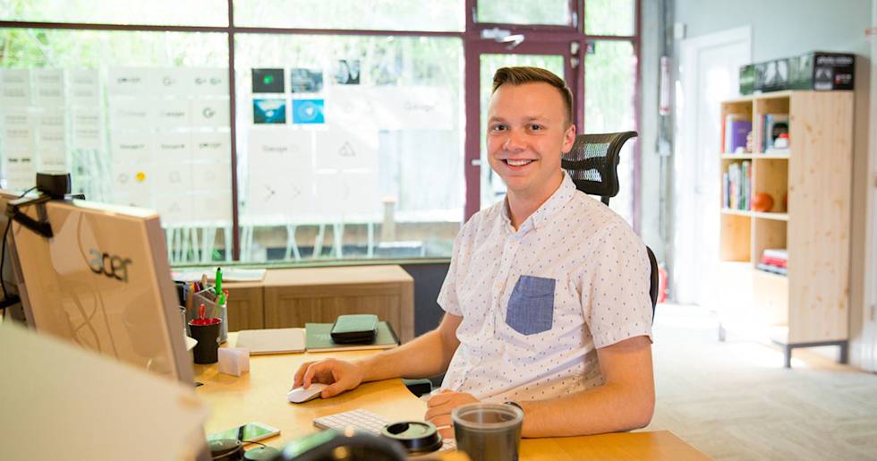 Professional in white polka dot shirt working at modern office desk with Acer laptop, keyboard and coffee cup nearby