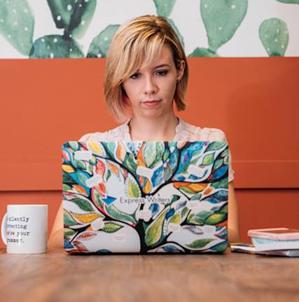 A photo of Julia McCoy sitting at a table with an open laptop in front of her.