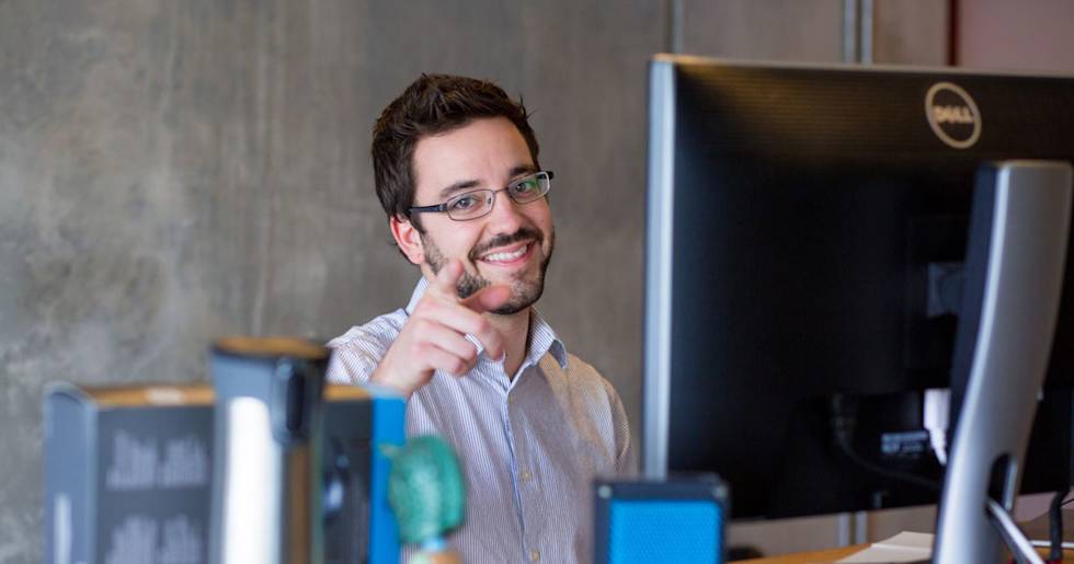 Professional in glasses and striped shirt smiling thoughtfully at workstation with Dell monitor in modern office setting