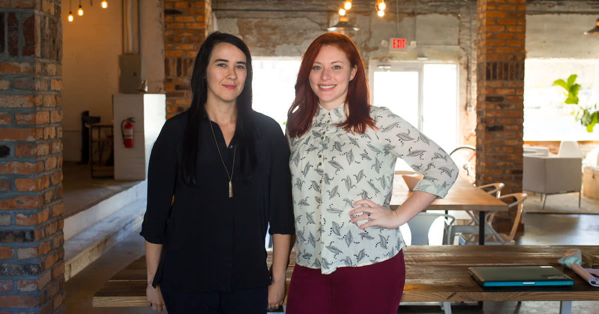 Two professionals standing in modern office space with exposed brick walls, pendant lighting, and wooden furniture