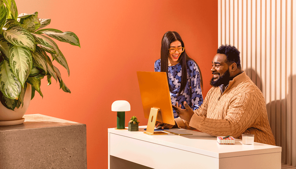 Two cheerful colleagues looking at a computer monitor