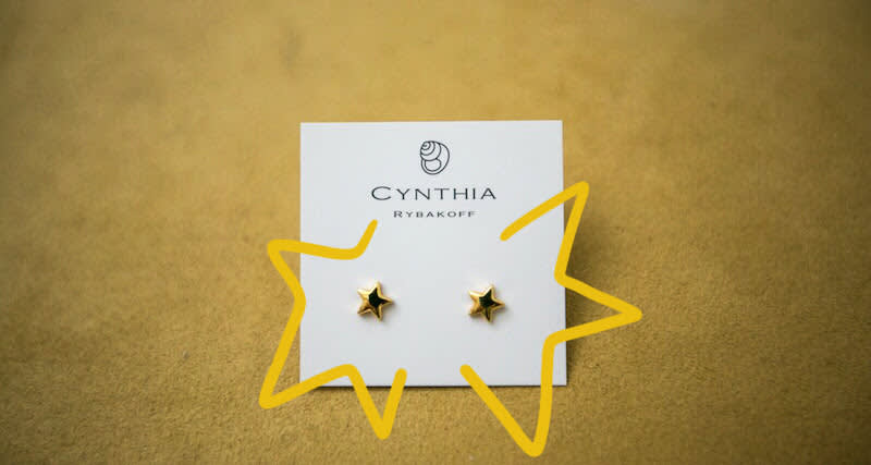 Gold star stud earrings displayed on white jewelry card with yellow star-shaped border against golden background