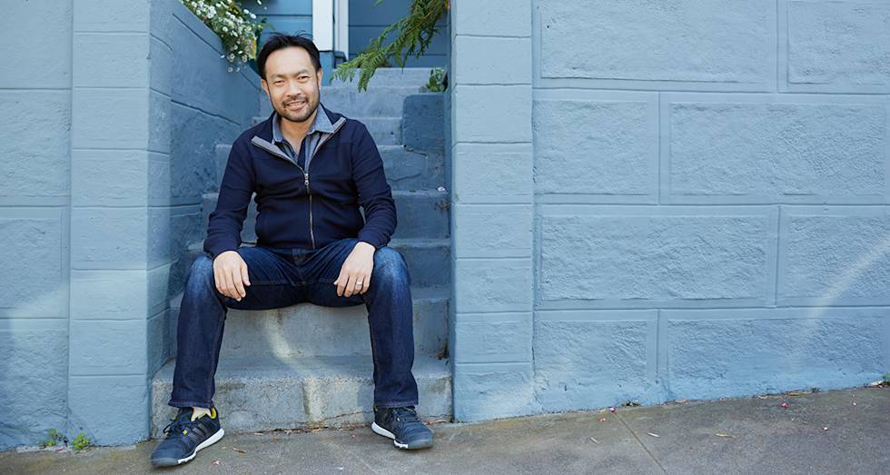Person in navy zip-up sweater and jeans sitting on light blue concrete steps against matching painted wall