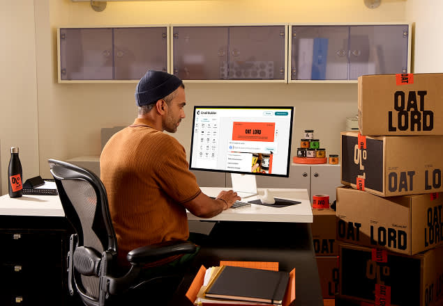 Designer in brown sweater working at desk surrounded by Oat Lord branded boxes and product packaging materials