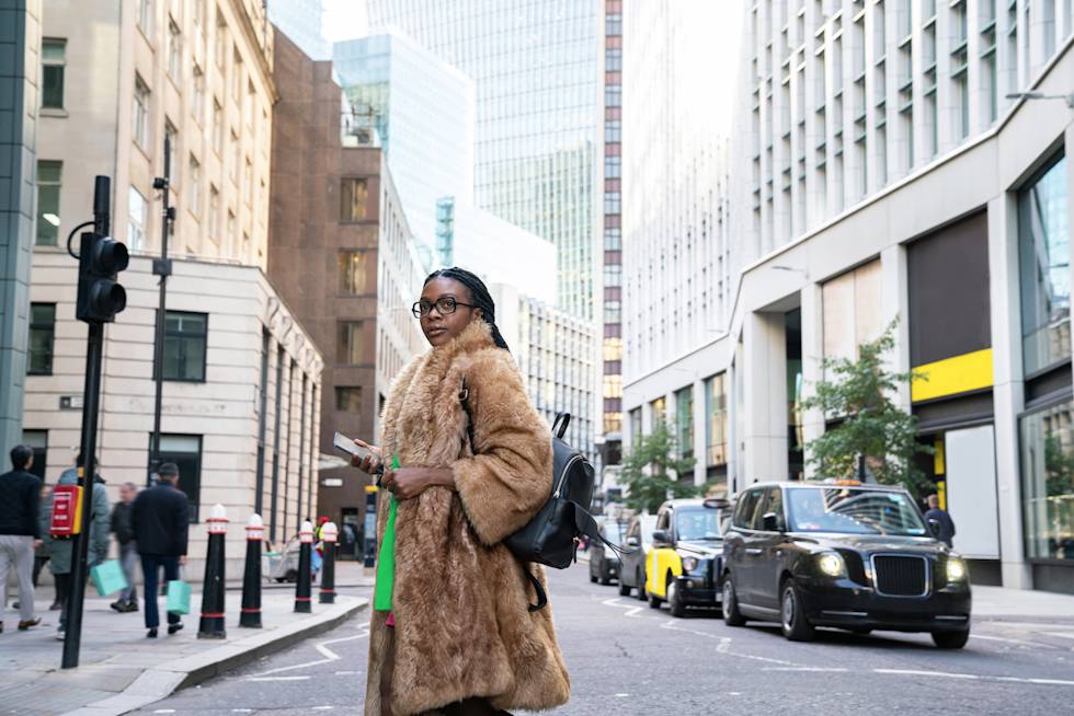 A stylish woman in a fur coat and green shirt confidently crossing a London street