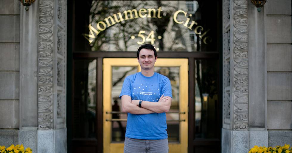 Person in blue conference t-shirt standing in front of Monument Circle 54 building entrance with yellow flowers below