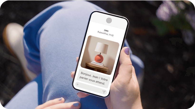 Image d'une personne tenant un smartphone affichant un SMS de la marque fictive Assembly. Le visuel illustre comment les entreprises peuvent augmenter leurs ventes grâce à l’automatisation des relances en cas de panier abandonné et rattraper les opportunités de vente perdues.