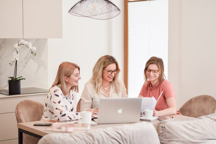 Three people working together at a bright modern office space with laptops, coffee cups and an orchid plant under pendant lighting