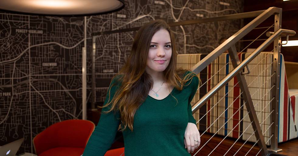 Professional in emerald green sweater standing by modern staircase with city map wall art and red chair in background