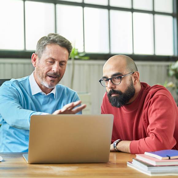 Man in blue and man in red looking at laptop