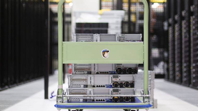 Server equipment stacked on a mint green cart with Mailchimp monkey logo in a data center environment