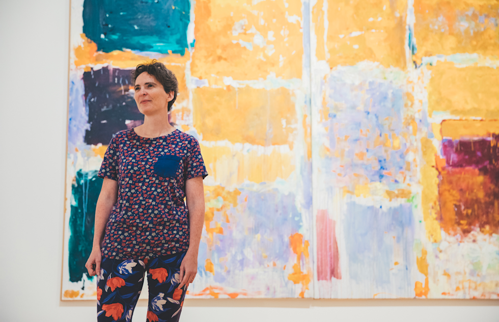 Hillary Brown stands in front of large abstract painting.