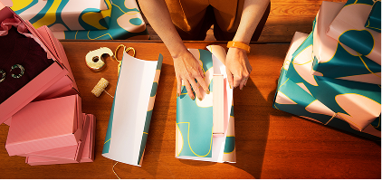 Hands arranging colorful paper documents and folders on a wooden desk surface, viewed from above