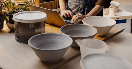Image of Intuit Mailchimp Customer Pottery West showing a person working on a computer behind multiple pieces of pottery