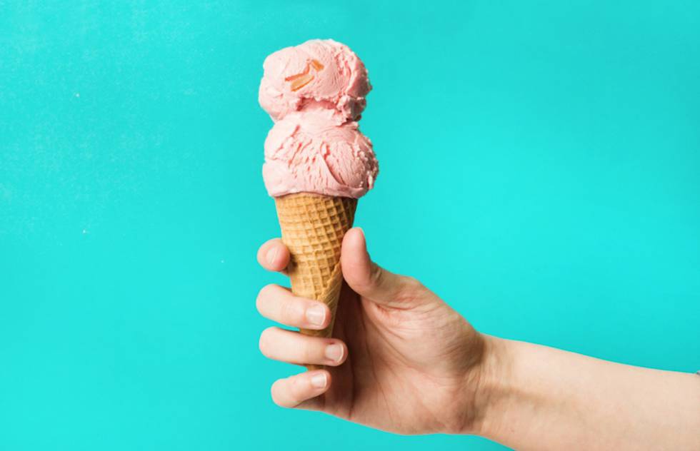 Hand holding a waffle cone with two scoops of pink ice cream against a bright turquoise background