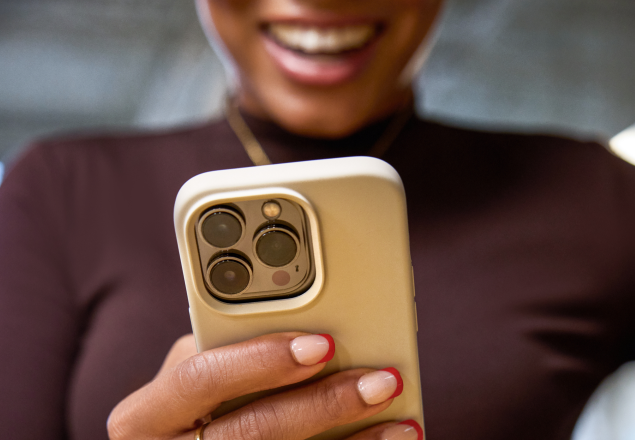 Close-up of hands holding a gold iPhone with triple camera, red nail polish visible on fingers