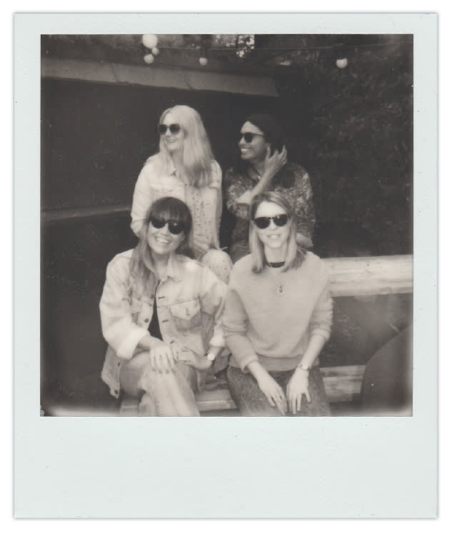 Black and white Polaroid photo of four friends wearing sunglasses, sitting and standing casually outdoors on a sunny day
