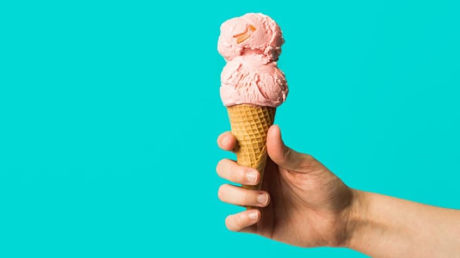 Hand holding a waffle cone with two scoops of pink ice cream against a bright turquoise background