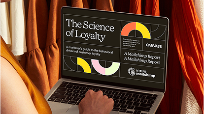 Laptop displaying "The Science of Loyalty" presentation with colorful geometric shapes on screen against orange fabric backdrop