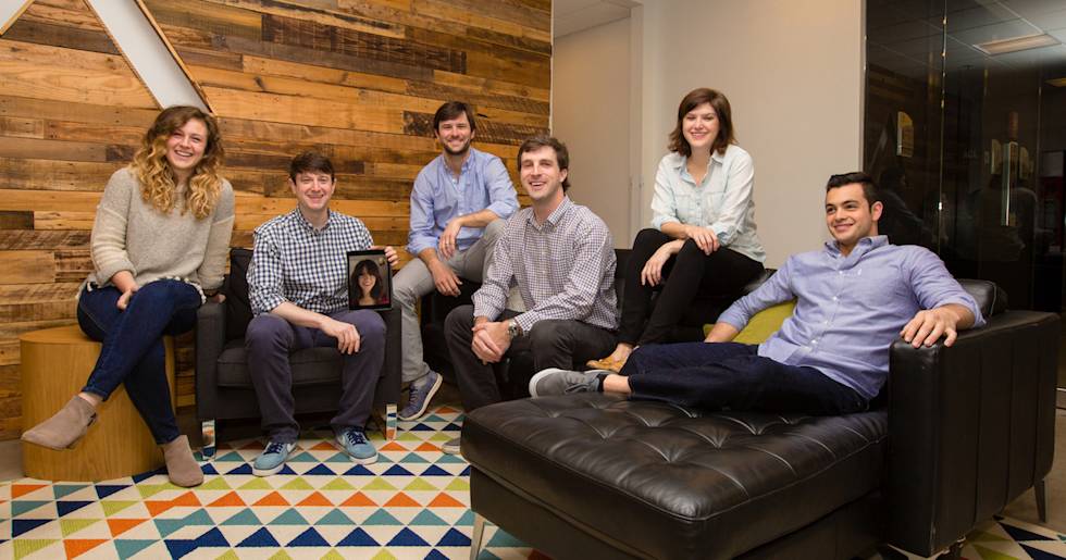 Team members relaxing in modern office lounge with wood accent wall, colorful geometric rug, and black leather furniture