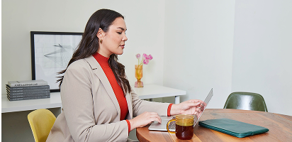 Professional in beige blazer and red turtleneck working at desk with tea and documents in modern office setting
