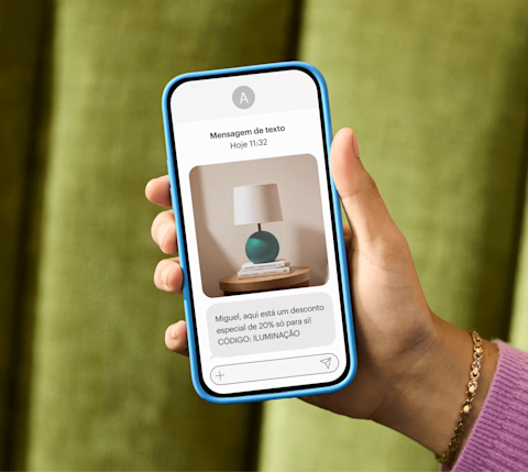 Mão exibindo um smartphone que acabou de receber uma mensagem de texto de marketing: "Alex, aqui está um desconto especial de 20% só para você!" CÓDIGO: ILUMINAÇÃO"
