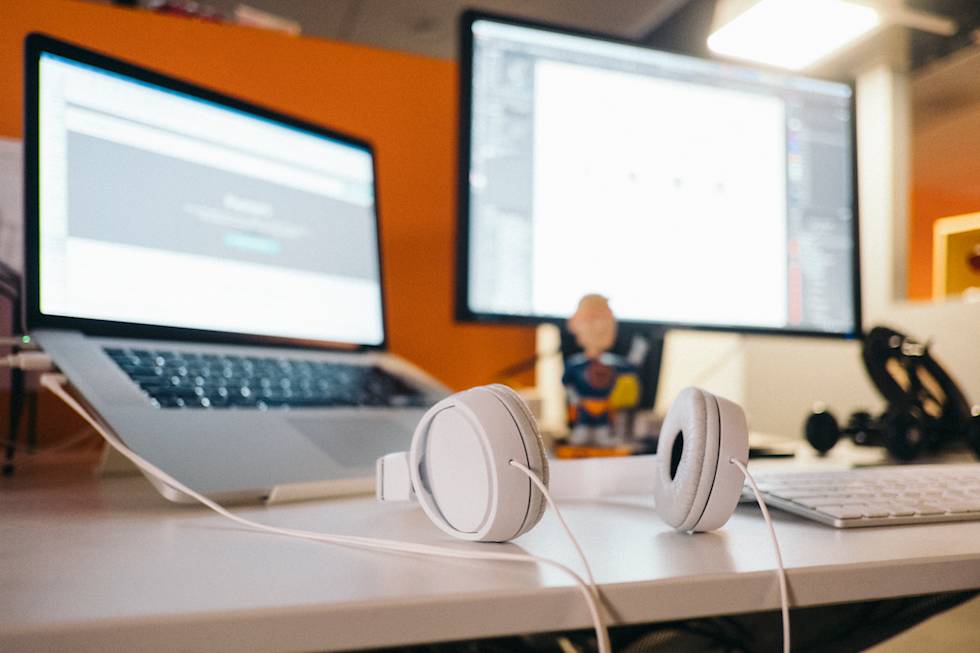 White headphones on desk with laptop and monitor against orange wall in modern workspace setup