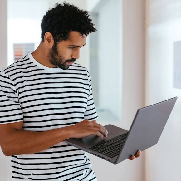 Man with striped shirt standing and holding laptop