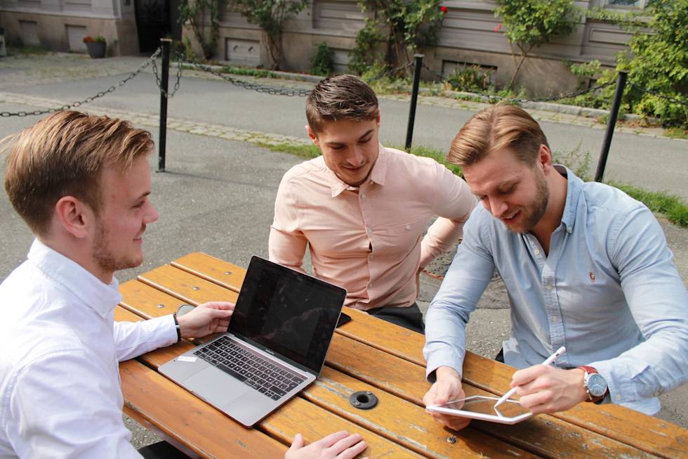 Leiv Kristian Steig and Ole Straume Andersen collaborate at outdoor wooden table with laptop and tablet, sharing ideas in casual business setting