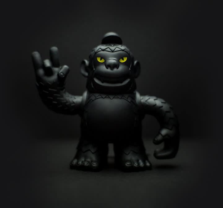 Black toy monster figurine with glowing yellow eyes waving against dark background