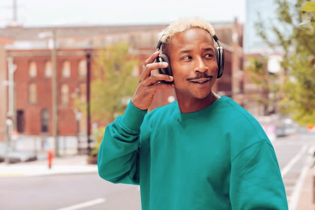 Person wearing green sweatshirt and headphones smiling while listening to music on city street