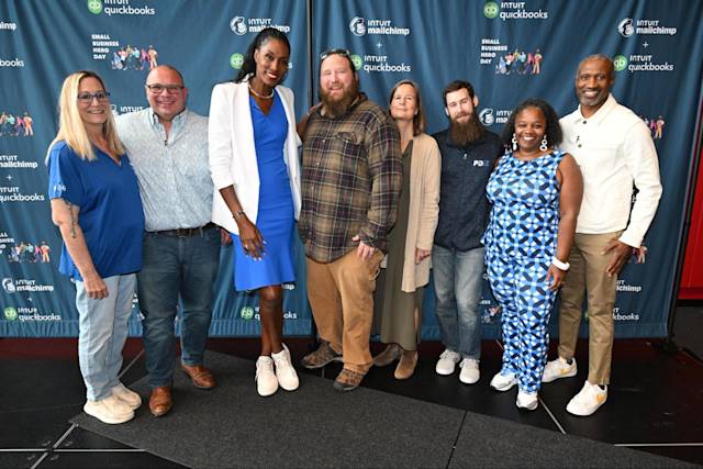 Group photo of eight people standing in front of Intuit QuickBooks and Mailchimp branded backdrop at Small Business Hero Day event