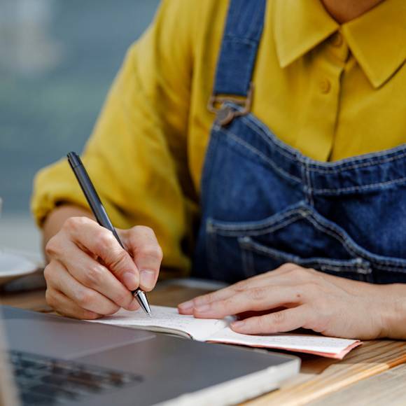 Person with yellow shirt and blue overalls writing with a pen