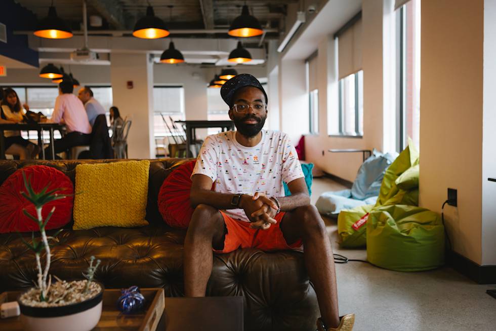 Person relaxing on leather couch in modern office lounge with colorful pillows and pendant lighting overhead