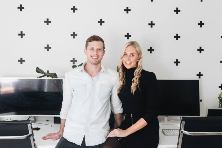 Two professionals in a modern office space with black plus sign wall decor, computer monitors, and minimalist furniture