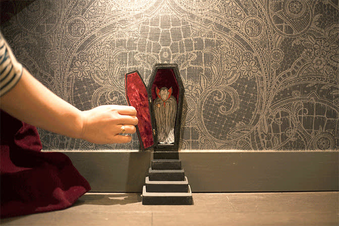 A hand opening a miniature coffin with Dracula inside