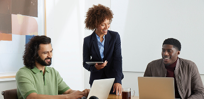 Three coworkers collaborating at a desk with laptops, sharing ideas and smiling during a casual office meeting