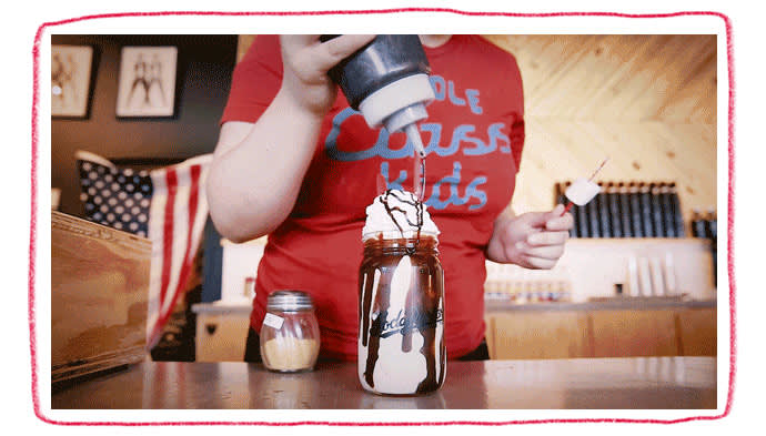 A lady adding chocolate drizzle to a milkshake