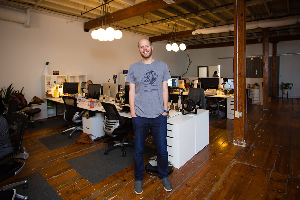 Modern open office space with wooden floors, exposed beams, globe lights, and white desks arranged in an open layout workspace.