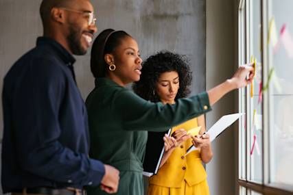 Three business professionals collaborating at a window, reviewing documents and placing sticky notes during a creative meeting