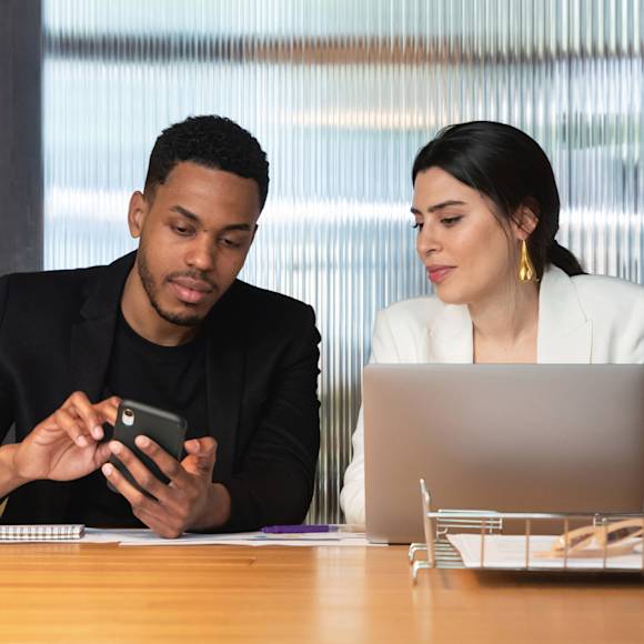 Co-workers discussing work on a phone and laptop