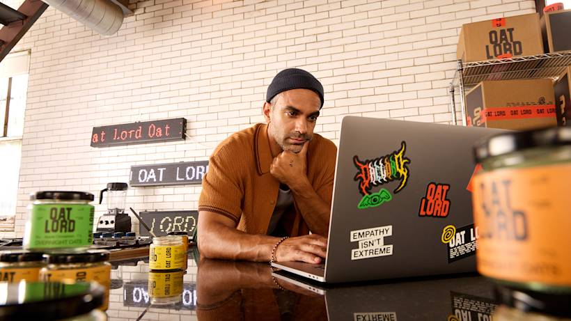 A person in a brown shirt and beanie works behind a counter with Oat Lord branded products and signage displayed throughout the space