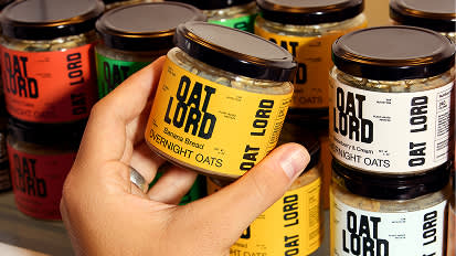 Glass jars with black lids containing oat products lined up on shelf, with yellow and black labels visible